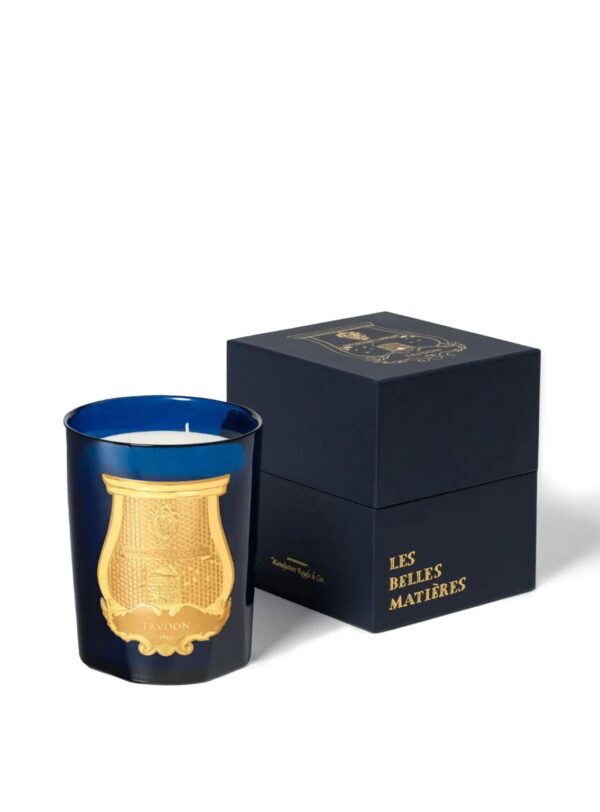 Vela Trudon Reggio en vaso azul con emblema dorado, presentada junto a caja azul marino Les Belles Matières.