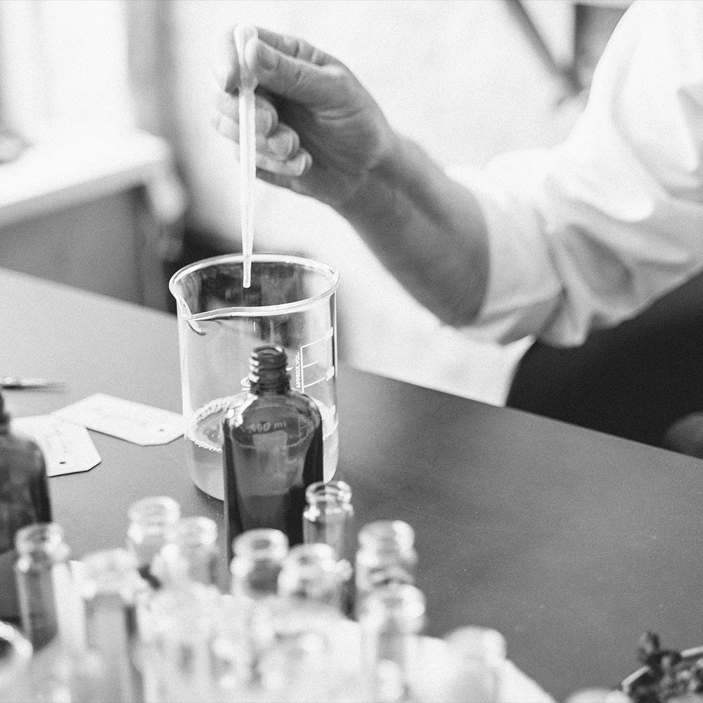 Mano con pipeta mezclando ingredientes en laboratorio de perfumería artesanal