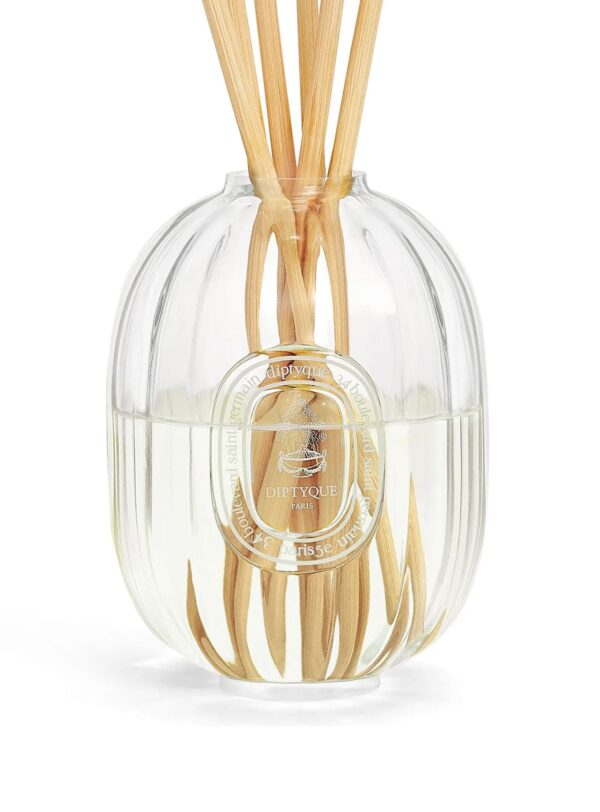 Difusor de fragancia Diptyque en vaso de cristal acanalado, con varillas de madera y líquido aromático en su interior.