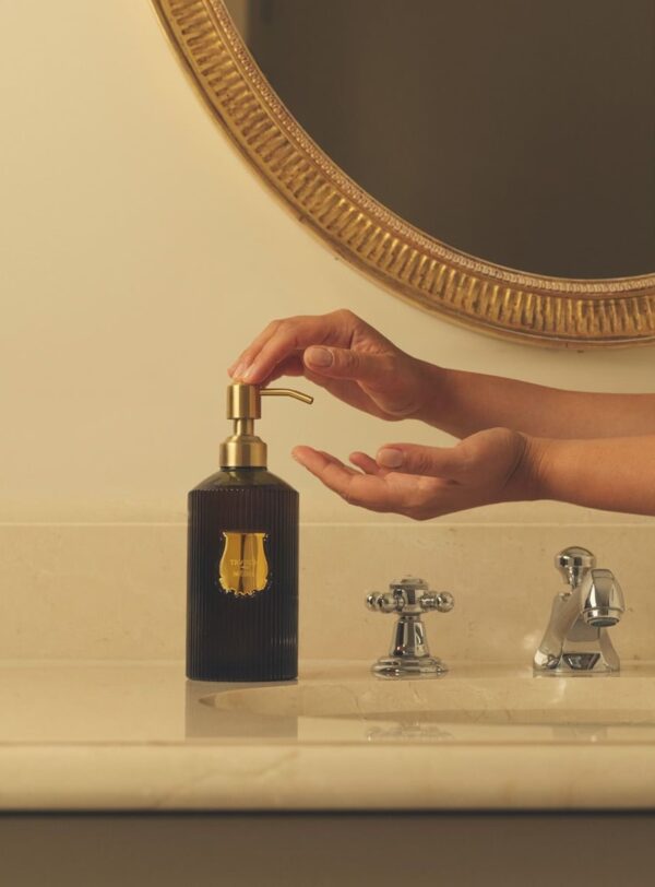 Jabón líquido Trudon Médie, frasco verde con bomba dorada colocado en baño elegante, manos aplicando el producto.