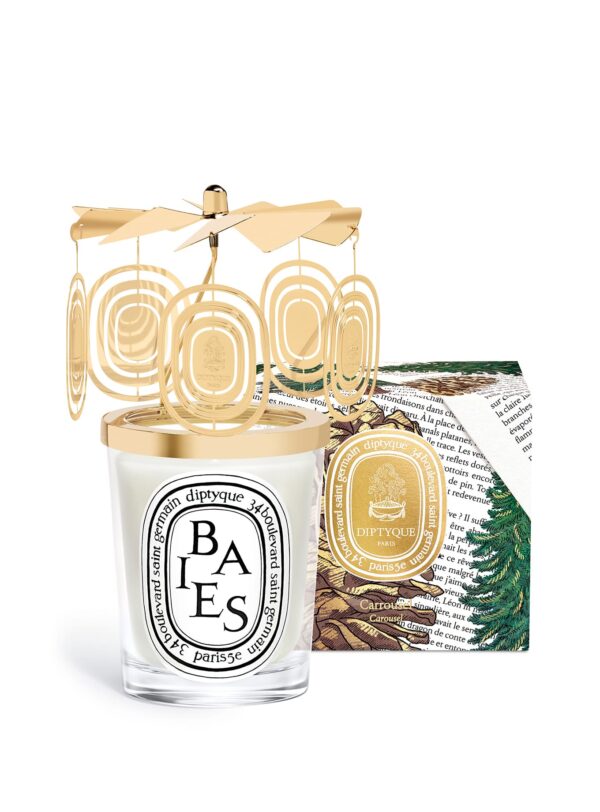 Diptyque Baies Carrousel Edición Limitada – vela con adorno dorado junto a caja decorada con pinos, aroma invernal.