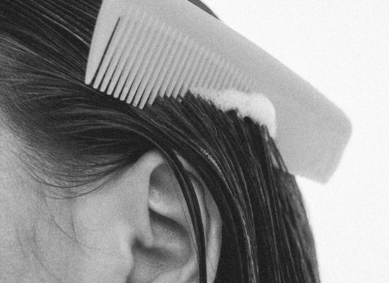 Primer plano en blanco y negro de una persona peinando su cabello mojado con espuma, ilustrando el uso de mascarillas capilares naturales recomendadas por Papaduk.
