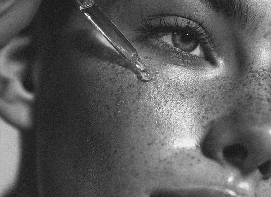 Close-up of a facial serum being applied with a dropper onto the skin of the face, showing texture and radiance in a skincare routine.